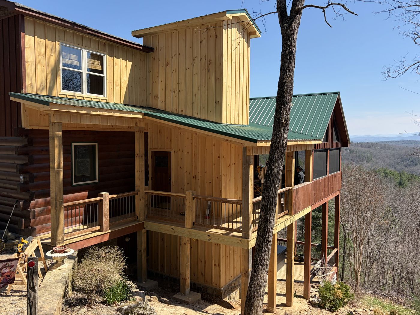 Mountain cabin with wraparound porch, board-and-batten siding, and a green metal roof set against a ridge view