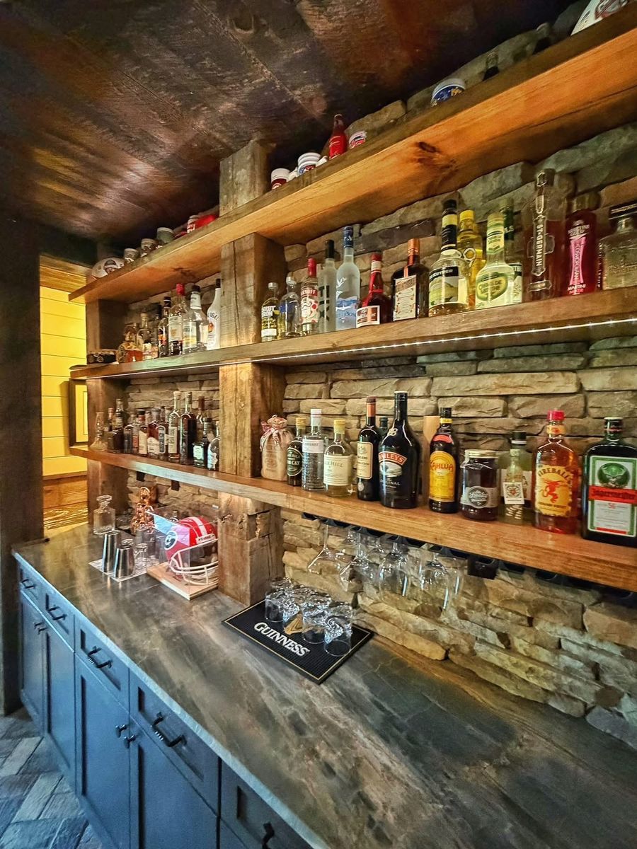 Custom basement bar with stacked stone wall, reclaimed-wood shelving, and recessed under-shelf lighting